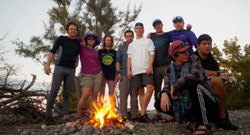 a group of outward bound students pose for a photo beside a campfire 